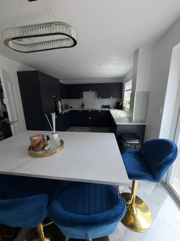 Modern navy blue kitchen with marble countertops, gold hardware, and blue velvet bar stools after professional cleaning