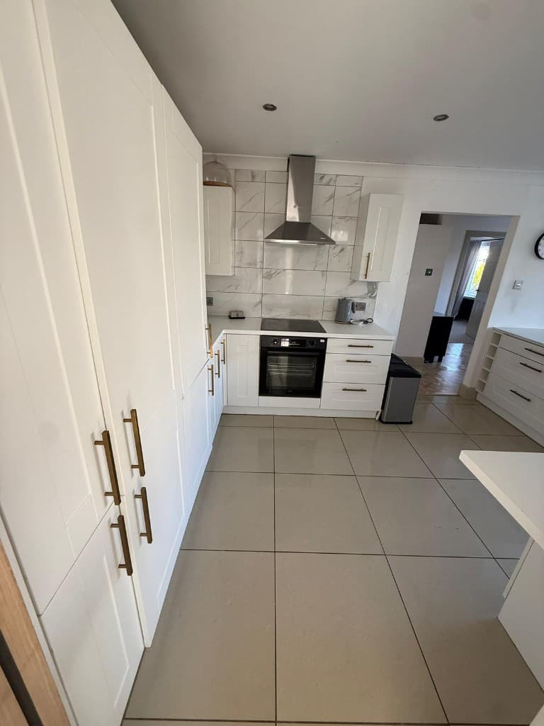 Bright white shaker kitchen with gold handles, marble-effect backsplash, and polished surfaces after end-of-tenancy cleaning