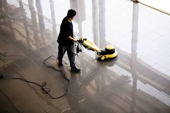 Professional cleaner in blue scrubs mopping a polished corridor floor with a janitorial trolley in a bright commercial building
