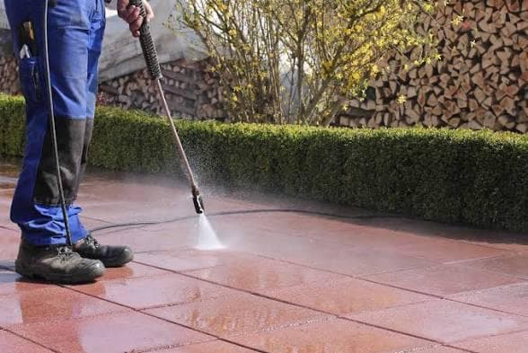 Cleaner pressure washing terracotta patio tiles with a high-pressure lance in a residential garden setting