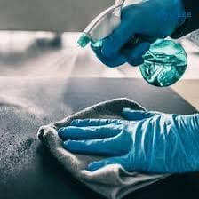 Two cleaners wearing blue gloves spraying disinfectant mist onto a stainless steel work surface during professional sanitisation